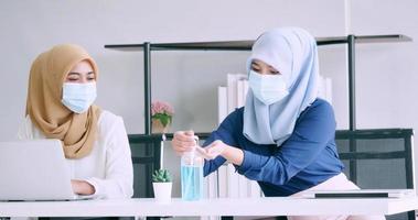 empresárias muçulmanas usam máscaras protetoras e limpam as mãos com álcool gel desinfetante durante o trabalho no escritório. foto