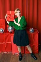mulher elegante elegante madura com caixa de presente em fundo vermelho. festa, moda, celebração, conceito anti-idade. foto