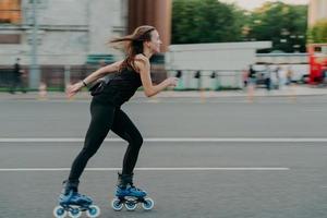 conceito de lazer ativo. tiro de comprimento total de patins de jovem magro ao longo do asfalto na rua gosta de velocidade passa o tempo livre em poses de passatempo favorito ao ar livre respira ar fresco. andar de patins foto