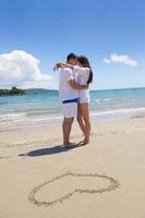 casal romântico apaixonado se diverte na praia com desenho de coração na areia foto