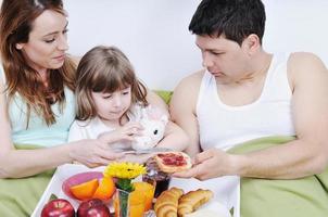 família jovem feliz toma café da manhã na cama foto