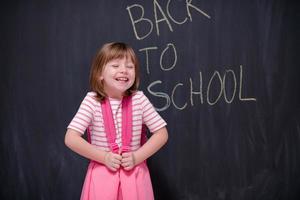 menina da escola com mochila escrevendo lousa foto