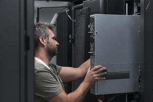 engenheiro de TI trabalhando na sala de servidores ou data center, o técnico coloca em um rack um novo servidor de supercomputador de mainframe de negócios corporativos ou fazenda de mineração de criptomoeda. foto