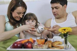 família jovem feliz toma café da manhã na cama foto