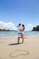 casal feliz se diverte na praia com coração na areia foto