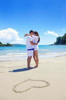 casal romântico apaixonado se diverte na praia com desenho de coração na areia foto