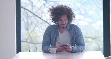 jovem tomando café e usando um celular em casa foto