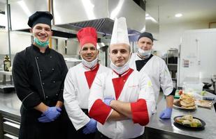 chefs de grupo juntos na cozinha do restaurante usando máscara médica protetora e luvas no novo conceito normal de coronavírus foto