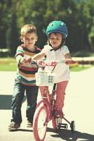 menino e menina no parque aprendendo a andar de bicicleta foto