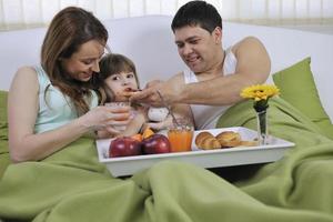 família jovem feliz toma café da manhã na cama foto