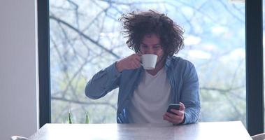 jovem tomando café e usando um celular em casa foto