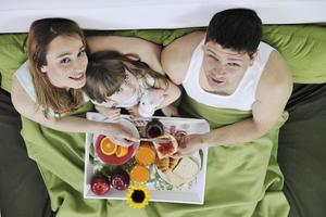 família jovem feliz toma café da manhã na cama foto