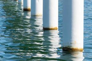 postes de cais enferrujados em água salgada do mar. colunas brancas diagonais. pilares de montagem para ponte. tempo ensolarado. foto