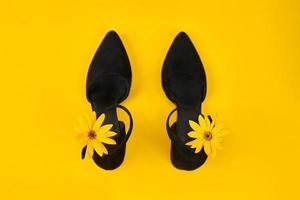 sapatos de camurça preta com botão de flor de topinambur amarelo na alça, fundo amarelo, sapatos da moda foto