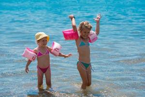 meninas com braçadeiras de natação brincando em águas rasas foto