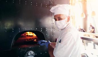 chef com máscara facial protetora de coronavírus preparando pizza foto