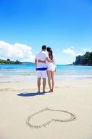 casal romântico apaixonado se diverte na praia com desenho de coração na areia foto