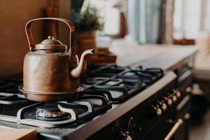 chaleira de alumínio velha fervendo no fogão a gás na cozinha contra aconchegante fundo desfocado. item antigo feito de metal cobre. estilo vintage foto