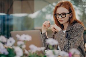 jovem empresária ruiva focada trabalha on-line no café ao ar livre foto