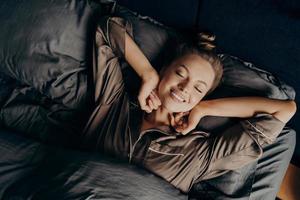 jovem linda morena relaxada em pijama de cetim, estendendo-se na cama foto
