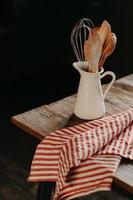 tiro vertical de utensílios de cozinha vintage em pote de cerâmica branca na mesa de madeira. decoração de cozinha em casa. utensílios de cozinha para cozinhar. coisas de casa foto
