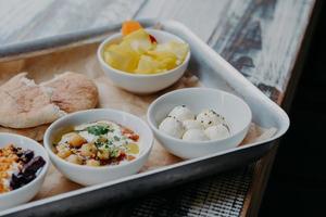 conceito de prato tradicional saboroso. foto recortada de bandeja com queijo de cabra, pão pita, beterraba grelhada em tigelas na mesa de madeira. comida israel