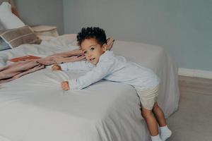 doce garotinho afro-americano brincando no quarto aconchegante em casa foto