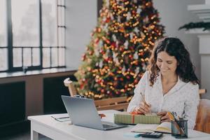 trabalhadora de escritório de mulher europeia satisfeita escrevendo carta de natal, cartão de felicitações com desejos de férias