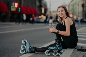 pessoas atividades ao ar livre e conceito de recreação. foto horizontal de mulher magra ativa estar em boa forma física anda de patins usa smartphone envia mensagens de texto online poses fora