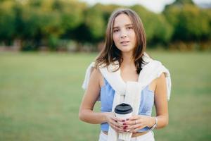 modelo feminino bonito tem cabelo escuro, vestido com roupas casuais, tem manicure, tem café para viagem, gosta de clima quente ensolarado, natureza bonita, tempo de recreação, conversas com amigos fazem piquenique juntos foto