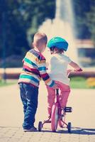 menino e menina no parque aprendendo a andar de bicicleta foto