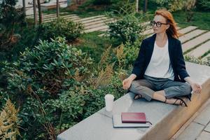 mulher ruiva relaxada medita no parque tem meditação pacífica gosta da natureza foto