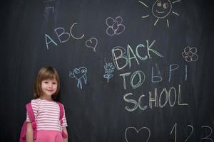 menina da escola com mochila escrevendo lousa foto