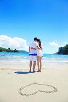 casal romântico apaixonado se diverte na praia com desenho de coração na areia foto