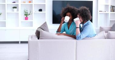 casal multiétnico sentado no sofá em casa bebendo café foto