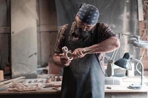 mestre de artesanato de colher em sua oficina com produtos artesanais de madeira e ferramentas trabalhando foto