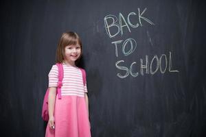 menina da escola com mochila escrevendo lousa foto