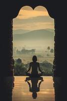 silhueta jovem praticando ioga no templo ao pôr do sol - efeito de cor estilo vintage foto