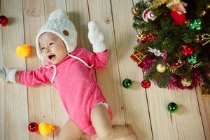 criança infantil com chapéu de poodle branco e luvas de malha e decoração de árvore de natal em fundo verde foto