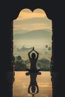 mulher de ioga sentada em pose de lótus no templo durante o nascer do sol, com reflexo no chão - efeito de cor de estilo vintage foto