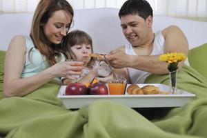 família jovem feliz toma café da manhã na cama foto