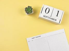 postura plana do livro rastreador de hábitos com vaso de plantas suculentas e calendário de madeira 01 de setembro em fundo amarelo. foto