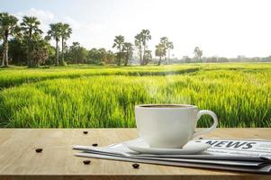 xícara de café com jornal na mesa de madeira e o fundo do campo de arroz foto