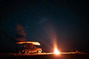 paisagem noturna com fogueira brilhante e carro foto
