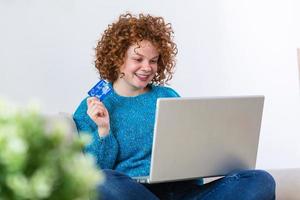 jovem segurando o cartão de crédito e usando o computador portátil. conceito de compras on-line. mulher feliz fazendo compras online em casa foto