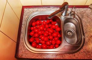 tomates vermelhos frescos são lavados em água na pia da cozinha. foto