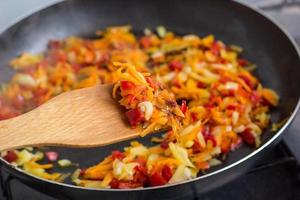 cozinhar um assado para sopa de cebola, cenoura, páprica, tomate, ervas e especiarias em óleo de girassol em uma frigideira foto
