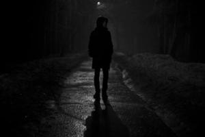 silhueta do homem à noite no parque. homem caminha sozinho na estrada à noite. foto