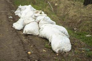 sacos brancos em uma estrada rural. reforçando o lado da estrada da inundação. lixo abandonado no lugar errado. foto