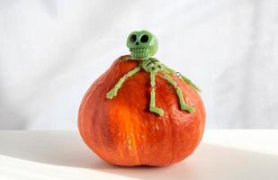 um esqueleto de brinquedo verde está sentado em uma abóbora laranja. o conceito de uma festa de halloween feliz foto